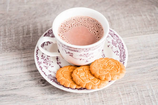 Cup of hot cocoa drink with vanilla flower shaped cookies on a dessert plate on a wooden table, selective focus. Food for breakfast.