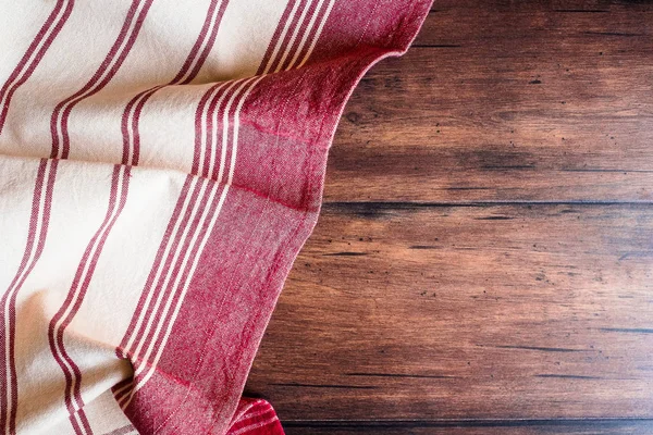 Striped red and white napkin on an old wooden brown background, top view. Image with copy space. Kitchen table with a towel - top view with copy space.