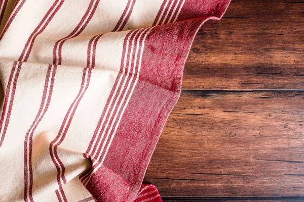 Striped red and white napkin on an old wooden brown background, top view. Image with copy space. Kitchen table with a towel - top view with copy space.