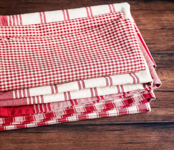 Stacked red checkered, red and white striped napkins on an old wooden brown table, selective focus. Image with copy space. Kitchen table with towels.