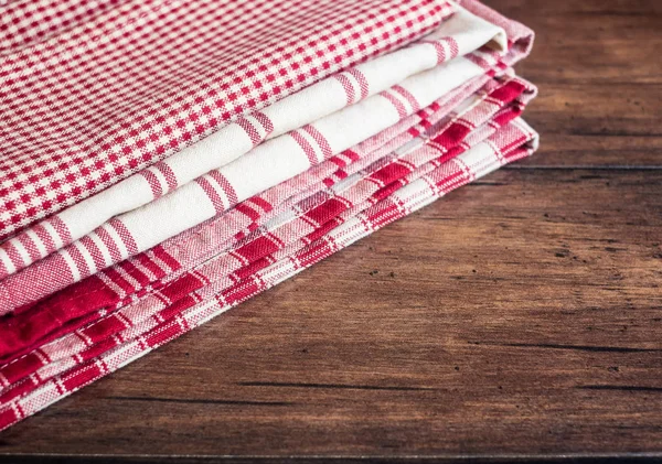 Stacked red checkered, red and white striped napkins on an old wooden brown table, selective focus. Image with copy space. Kitchen table with towels.