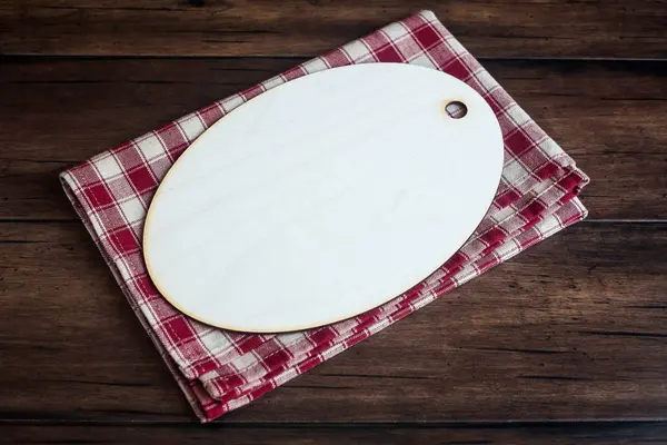 Empty wooden cutting board on a checkered red napkin on an old wooden brown background, top view. Image with copy space. Kitchen table with a towel and a board - top view with copy space.