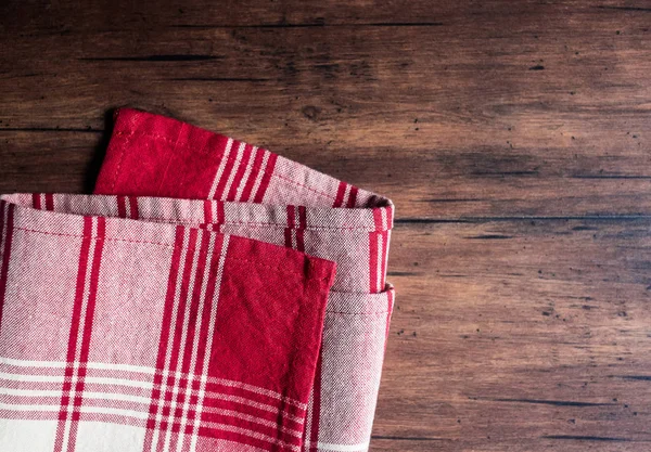 Striped red and white napkin on an old wooden brown background, top view. Image with copy space. Kitchen table with a towel - top view with copy space.