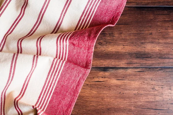 Striped red and white napkin on an old wooden brown background, top view. Image with copy space. Kitchen table with a towel - top view with copy space.