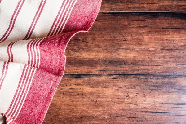 Striped red and white napkin on an old wooden brown background, top view. Image with copy space. Kitchen table with a towel - top view with copy space.