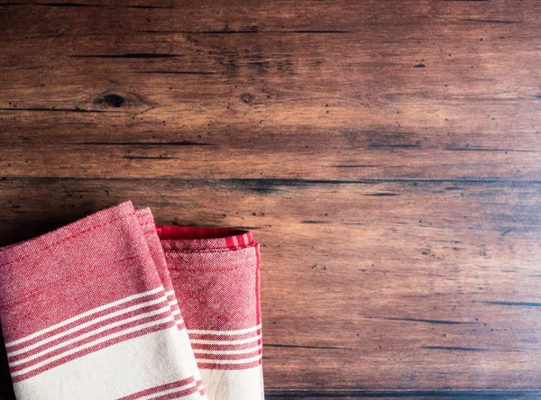 Striped red and white napkin on an old wooden brown background, top view. Image with copy space. Kitchen table with a towel - top view with copy space.