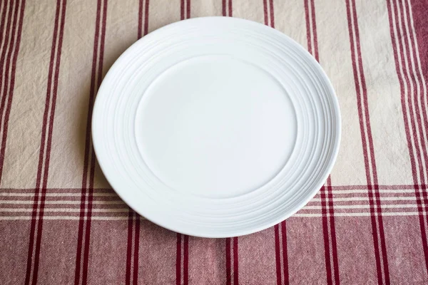 Empty white plate on a napkin on an old wooden brown background, top view. Image with copy space. Kitchen table with a towel and a plate - top view with copy space.