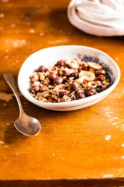 Organic granola or muesli with oat flakes, dried fruits and nuts in a bowl for breakfast on a wooden table, selective focus