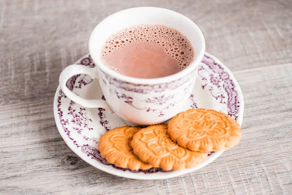 Cup of hot cocoa drink with vanilla flower shaped cookies on a dessert plate on a wooden table, selective focus. Food for breakfast. Christmas food.