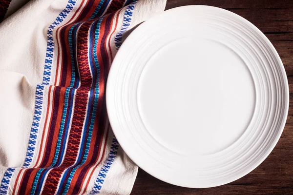 Empty white plate on a napkin, top view. Image with copy space. Kitchen table with a towel and a plate - top view with copy space.