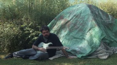 Dışarıda gitar çalan evsiz bir müzisyen var.