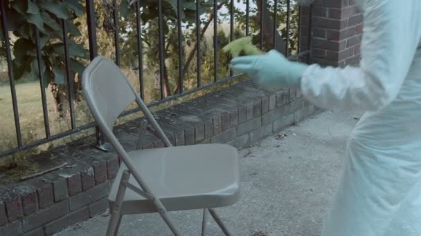 Koronavirüs Yüzünden Sandalyeye Sprey Sıkan Ppe Kıyafetli Bir Adam — Stok video