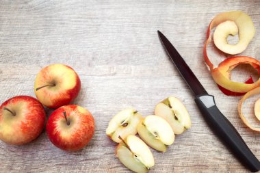 Olgunlaşmış kırmızı elmalar ve ahşap masa zemininde bıçakla soyulmuş kabuklar. Metin için fotokopi alanı olan taze meyve arkaplanı. Dilimlenmiş meyve, pişirme konsepti