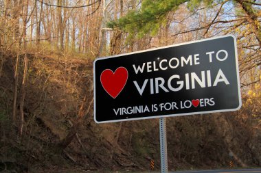 A roadside sign welcomes travelers along a rural road to the state of Virginia clipart