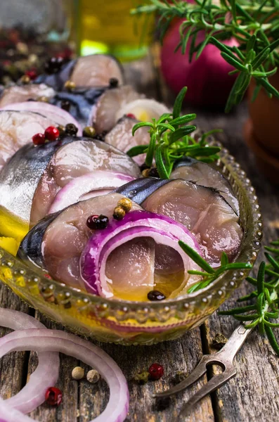 Marinated fish slices with onions and spices in a dish on a wooden background. Selective focus.