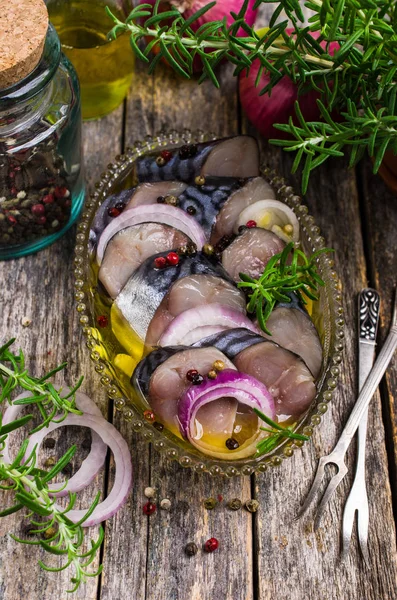 Marinated fish slices with onions and spices in a dish on a wooden background. Selective focus.