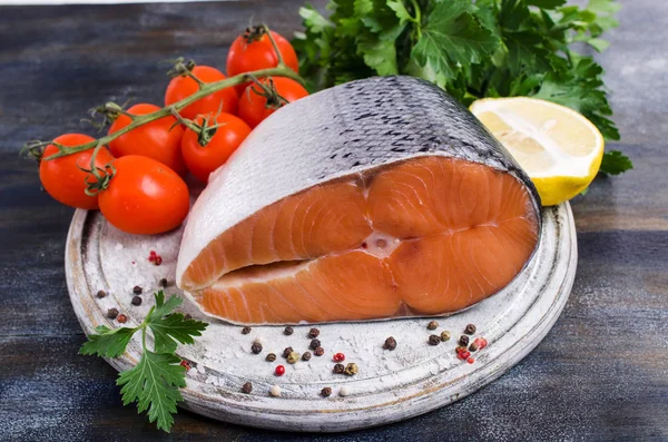 Slice of raw salmon in scales with vegetables and spices on a dark wooden background. Selective focus.