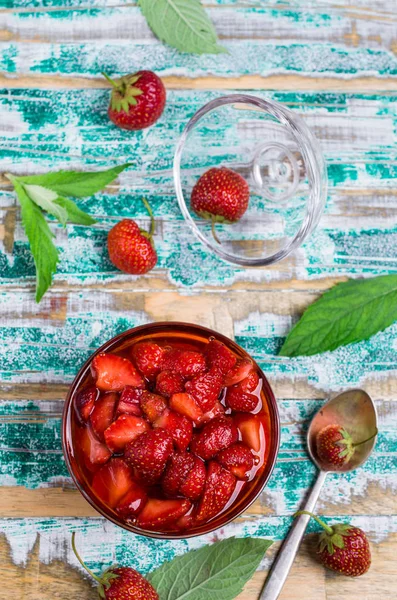 Slices of red strawberries with syrup in a glass jar on a wooden table. Selective focus.