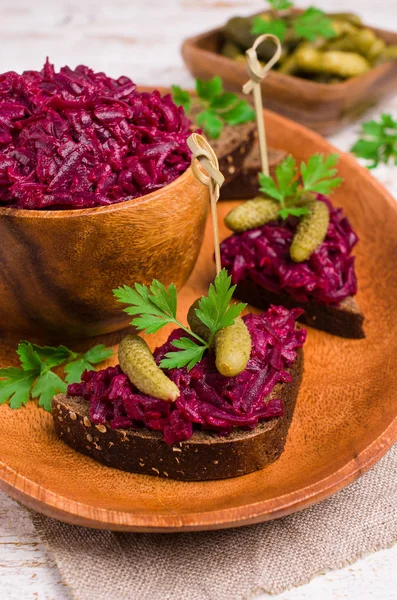 Sandwiches with beet and pickled cucumber on dark bread on a wooden background. Selective focus.