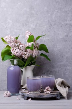 Gri arka planda bir bardakta leylak içkisi. Seçici odak.