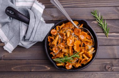 Koyu ahşap zemin üzerinde soğanlı ve biberiyeli mantar kızartması. Seçici odak.