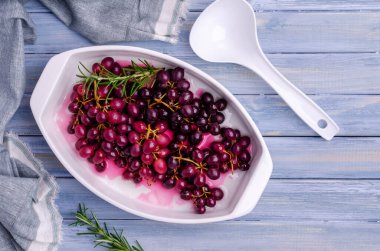 Mavi ahşap arka planda seramik bir tabakta biberiyeli koyu üzüm demetleri. Seçici odak.