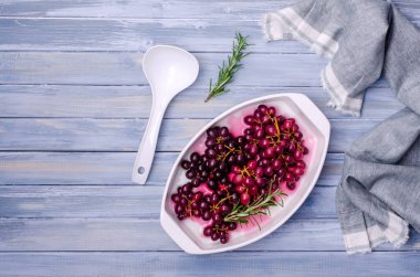 Mavi ahşap arka planda seramik bir tabakta biberiyeli koyu üzüm demetleri. Seçici odak.