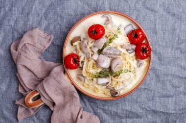 Mavi tekstil arka planında beyaz soslu mantarlı ve domatesli geleneksel makarna. Seçici odak.