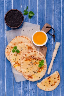 Geleneksel yassı ekmek, yağ, susam ve mavi ahşap arka planda naneli. Seçici odak.