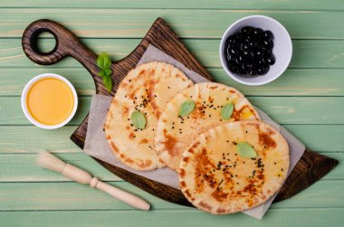 Yeşil ahşap arka planda yağlı, susamlı ve fesleğenli geleneksel yassı ekmek. Seçici odak.