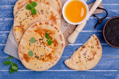 Geleneksel yassı ekmek, yağ, susam ve mavi ahşap arka planda naneli. Seçici odak.