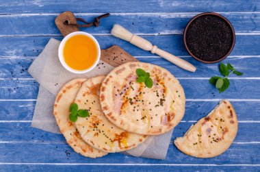 Geleneksel yassı ekmek, yağ, susam ve mavi ahşap arka planda naneli. Seçici odak.