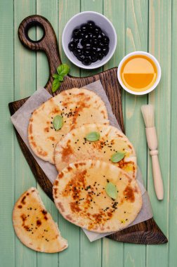 Yeşil ahşap arka planda yağlı, susamlı ve fesleğenli geleneksel yassı ekmek. Seçici odak.