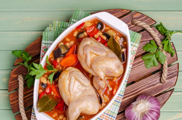 Stewed poultry with vegetables and beans in a dish on a green wooden background. Selective focus.