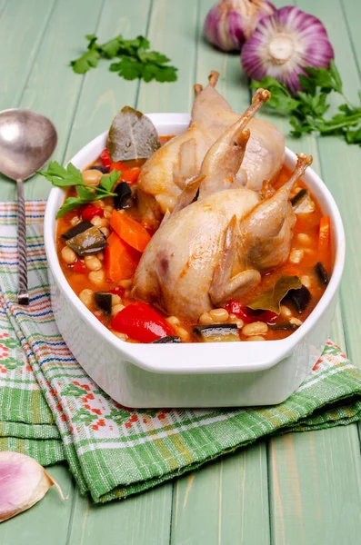 Stewed poultry with vegetables and beans in a dish on a green wooden background. Selective focus.
