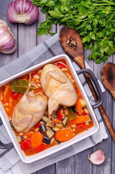 Stewed poultry with vegetables and beans in a dish on a gray wooden background. Selective focus.