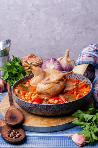 Stewed poultry with vegetables and beans in a dish on a blue wooden background. Selective focus.