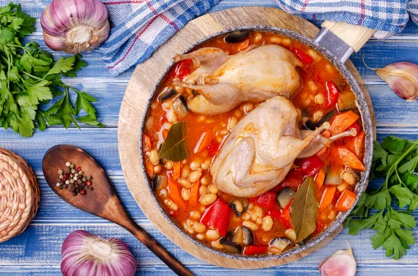 Stewed poultry with vegetables and beans in a dish on a blue wooden background. Selective focus.