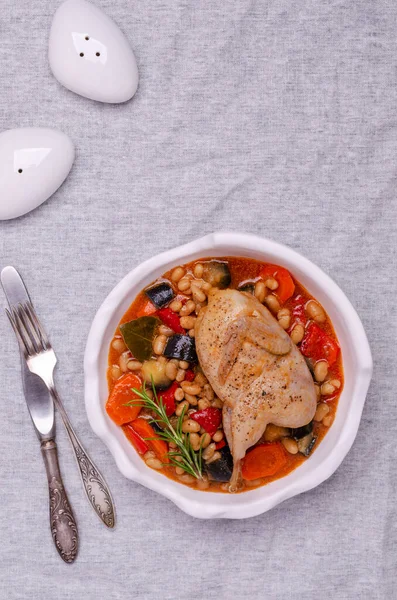 Stewed poultry with vegetables and beans in a dish on a textile background. Selective focus.