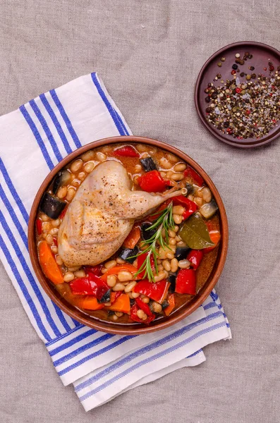 Stewed poultry with vegetables and beans in a dish on a textile background. Selective focus.