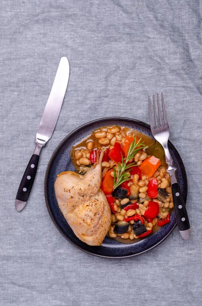 Stewed poultry with vegetables and beans in a dish on a textile background. Selective focus.