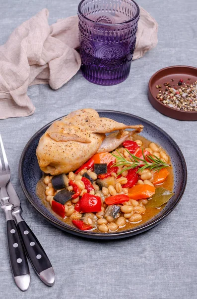 Stewed poultry with vegetables and beans in a dish on a textile background. Selective focus.