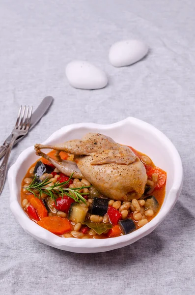 Stewed poultry with vegetables and beans in a dish on a textile background. Selective focus.