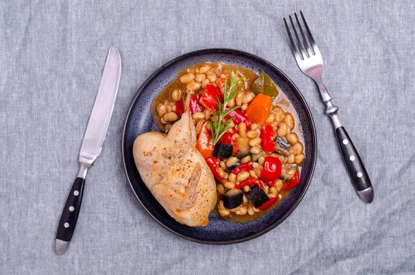 Stewed poultry with vegetables and beans in a dish on a textile background. Selective focus.