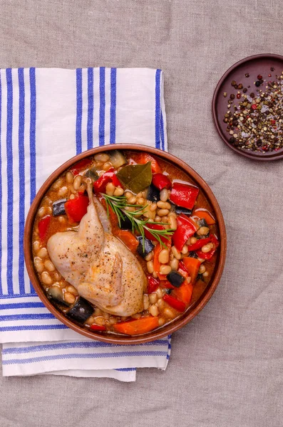 Stewed poultry with vegetables and beans in a dish on a textile background. Selective focus.