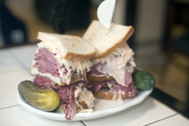 Kosher deli combination sandwich pastrami corned beef tongue cole slaw and Russian dressing on seeded Jewish rye bread with garlic and sour pickles New York restaurant delicatessen clipart