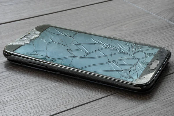 Broken smartphone on the floor. The screen is cracked and the phone is damaged.