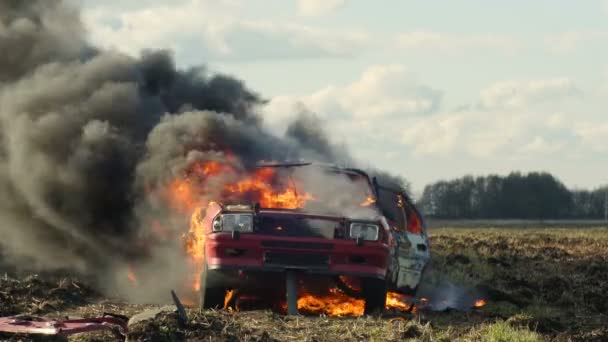 L'auto brucia nel campo e la sua ruota esplode. Auto in fiamme. Vista laterale . — Video Stock