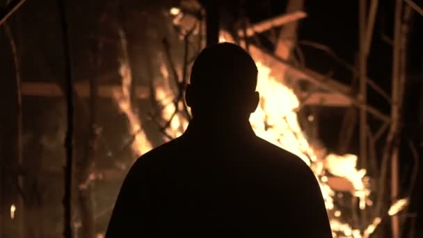 Мужчина стоит у горящего дома, мужчина против горящего дома ночью — стоковое видео