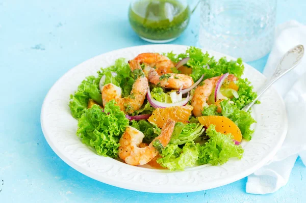 A plate of lettuce, with slices of orange, red onions, and prawns with vinaigrette dressing. A dietary dish.